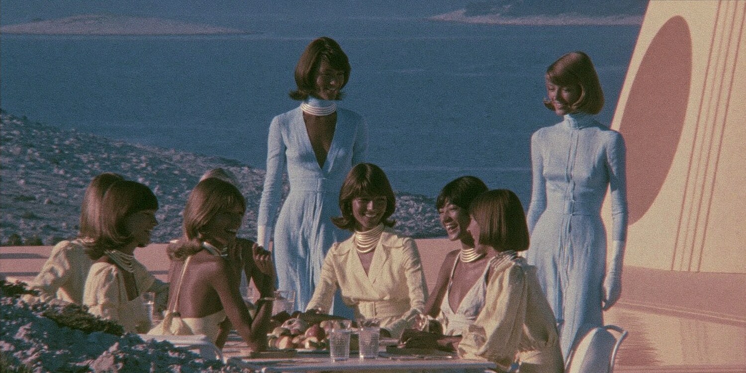 Seven of the crew at a long table above the water, all dressed alike.